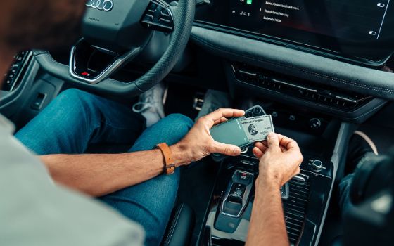 Ansicht einer silbernen Kreditkarte von American Express über einer Konsole in den Händen eines Mannes auf dem Fahrersitz eines modernen Autos