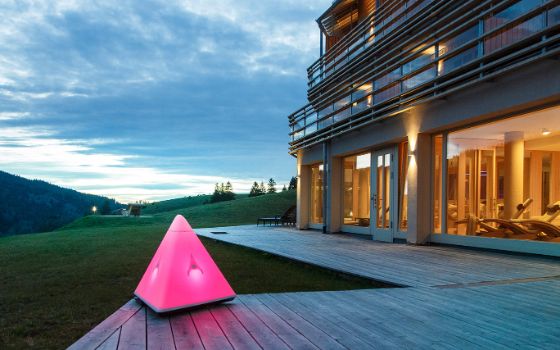 Ein Haus mit Glasfront und Holzterrasse steht in einer Berglandschaft.