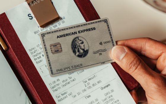 Eine Hand hält eine silberne Kreditkarte von American Express auf einer Restaurantrechnung in einem edlen Etui.