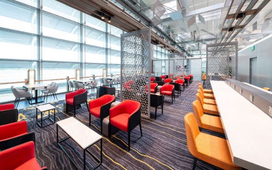 Menschenleere, lichtdurchflutete Flughafen-Lounge mit modernem Interieur und Sitzmöbeln in unterschiedlichen Farben. 