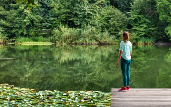 Frau steht auf einem Holzsteg am Weiher, umgeben von Seerosen und dichter grüner Vegetation, Blick auf das ruhige Wasser der Drei Weieren in St. Gallen.