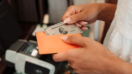 Eine weibliche Hand zieht eine silberne Kreditkarte von American Express aus einem Lederetui über einem Kartenlesegerät auf der Theke einer Boutique.