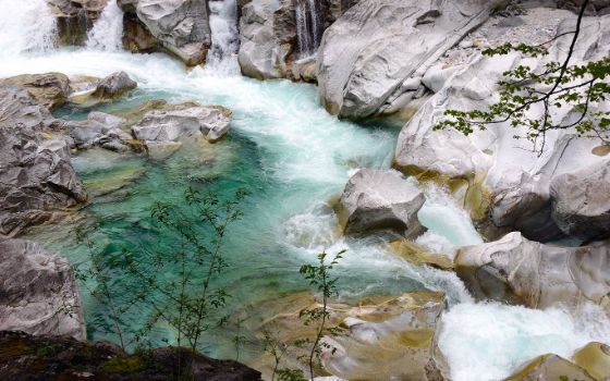Im Maggiatal fliesst ein Fluss zwischen den Steinen, an einigen Felsen kommen Wasserspritzer empor. 