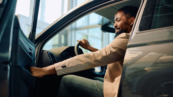 Ein Mann sitzt in einem schicken Auto und zieht lächelnd an der Fahrertür, um diese zu schliessen.