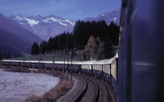 Aussenaufnahme eines blauen Zuges, der eine Kurve fährt in alpiner Landschaft bei Abenddämmerung.