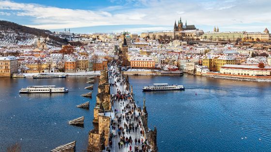 Winterliche Ansicht der Karlsbrücke in Prag mit Blick auf die verschneite Altstadt und die Prager Burg.