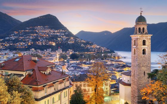 Blick über die Altstadt von Lugano mit der Kirche San Lorenzo, dem Lago di Lugano und dem Monte Brè bei Sonnenuntergang.