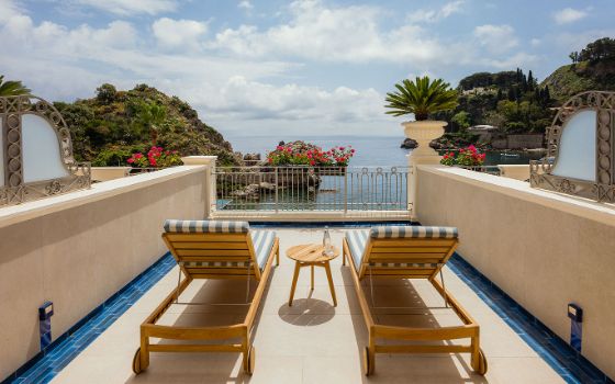 Rückansicht von zwei Sonnenliegen auf einer kleinen, privaten Hotelterrasse mit Blick aufs Meer an einer mediterranen Felsküste.