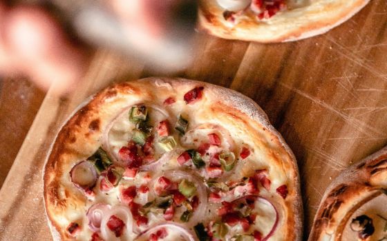 Traditioneller Elsässer Flammkuchen mit Speck, Zwiebeln und Rahm auf Holzbrett.