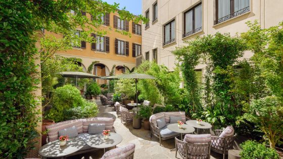 Sitzgarnituren mit Sonnenschirmen in einem begrünten Innenhof zwischen eleganten Hausfassaden bei Sonnenschein