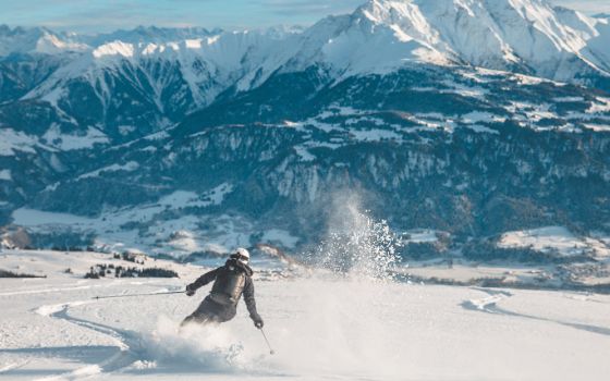 Vor einer schneebedeckten Berglandschaft fährt eine Person Ski im Schnee. 
