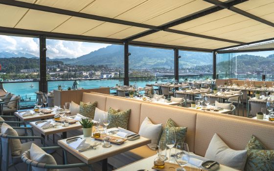Blick auf die Terrasse eines Restaurants, im Hintergrund der Ausblick auf einen See und ein Panorama mit Bergen und Stadt.  