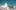 Zwei Skifahrende sitzen in einem Sessellift vor schneebedecktem Bergpanorama mit spitzer Felsformation unter blauem Himmel.