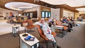 Mehrere Personen auf Ledersesseln in einer hellen, modernen Flughafen-Lounge.