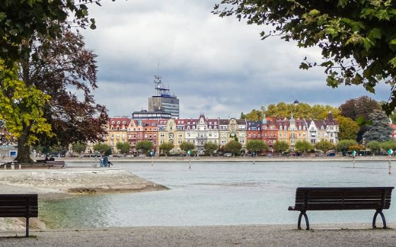 Blick vom Uferpark in Konstanz über den Seerhein auf eine Reihe historischer Häuser mit farbigen Fassaden, eingerahmt von Bäumen.