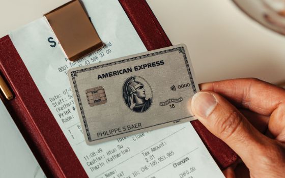 Nahaufnahme einer silbernen Kreditkarte von American Express, gehalten in einer Hand über einem Kassenbon in einer eleganten Rechnungsmappe.