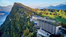 Auf einem grossen Berg steht direkt an einer Klippe ein Hotel mit vielen Fenstern. 