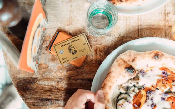 American Express Gold Card auf einem Tisch neben einem Teller mit Pizza