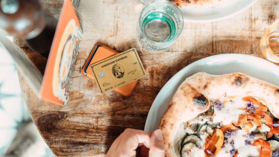 American Express Gold Card auf einem Tisch neben einem Teller mit Pizza