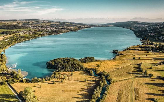 Türkisfarbener See in sanfter, grüner Hügellandschaft aus der Luftperspektive. 