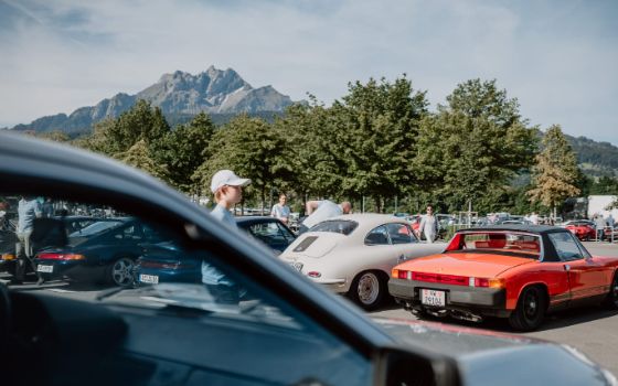 Verschiedene Oldtimer stehen auf einem Platz vor einer Bergkulisse.