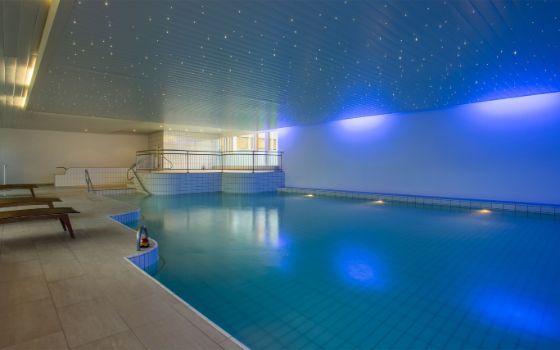Ein flacher Indoor-Pool mit Liegen und stimmungsvoller Beleuchtung in einem Wellnessbereich.