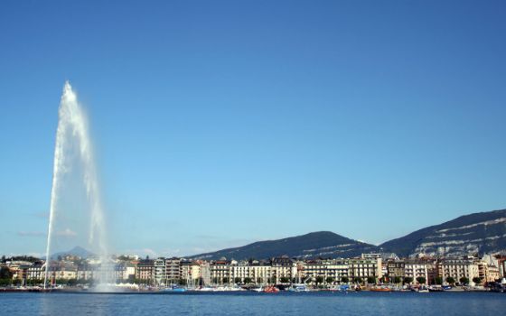 Jet d’Eau in Genf mit Blick über den Genfersee auf die Altstadt, Berge im Hintergrund und strahlend blauem Himmel.