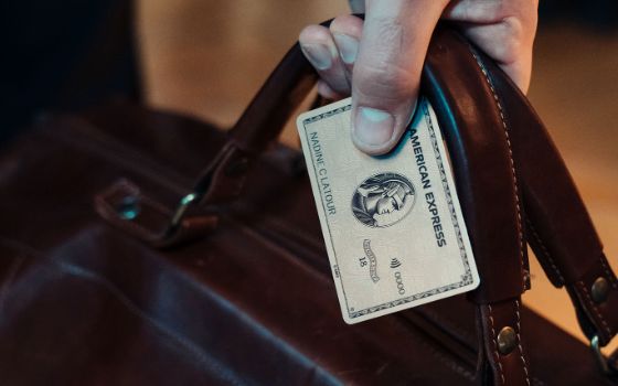 Nahaufnahme einer silbernen Kreditkarte von American Express in einer Hand, die gleichzeitig eine braune Ledertasche festhält.