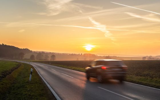 Rückansicht eines Autos in Bewegungsunschärfe auf einer Landstrasse bei Sonnenuntergang. 