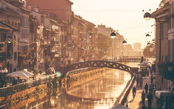 Abendstimmung im Navigli-Viertel in Mailand mit Blick auf den Kanal, gesäumt von historischen Häusern, Fussgängern und einer Brücke im warmen Licht der Sonne.
