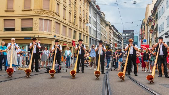 Alphornbläser in traditioneller Kleidung spielen in einer Stadt.