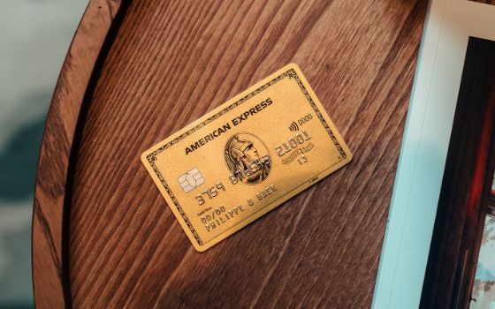 Nahaufnahme einer goldenen Kreditkarte von American Express auf einem runden Holztisch neben einer Zeitschrift 