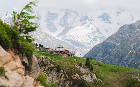 Umgeben von Bergen und grünen Pflanzen steht eine kleine Hütte mit Seilbahn. 