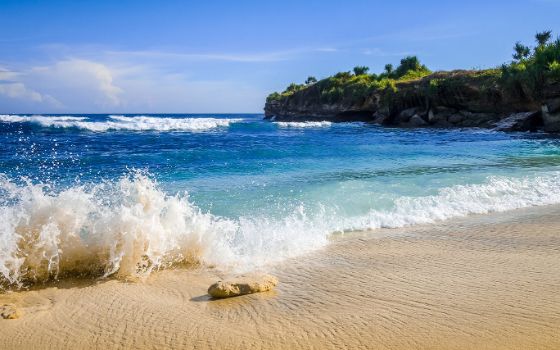 Ein weisser Strand mit blauem Meer und grünen Bergen.