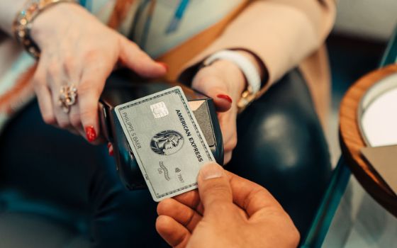 Kontaktlose Zahlung mit einer silbernen Kreditkarte von American Express in der Hand einer Person an einem Kartenlesegerät in den Händen einer elegant gekleideten Verkäuferin 