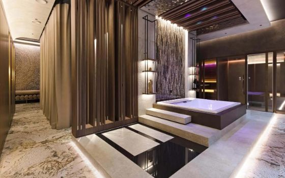 Ein grosser Raum eines Private Spas mit einem Jacuzzi und eleganter Einrichtung mit indirekter Beleuchtung und Steinboden.