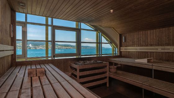 Eine geräumige Holzsauna mit Seeblick durch ein Panoramafenster.