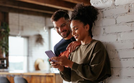 Eine Frau und ein Mann stehen in der Küche und schauen auf ein Smartphone.