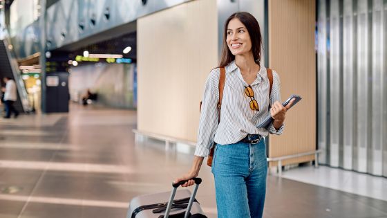 Eine Frau mit Rollkoffer läuft durch einen Flughafen. 