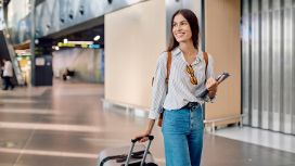 Eine Frau mit Rollkoffer läuft durch einen Flughafen. 