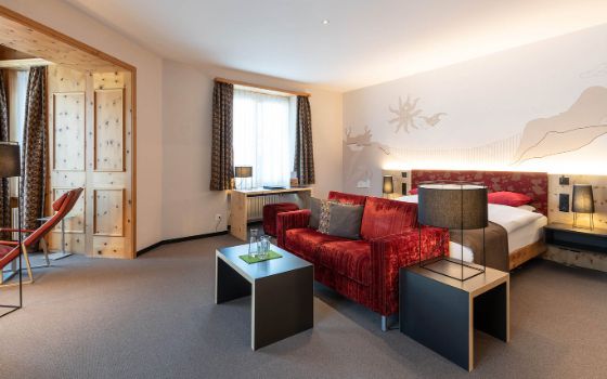 In einem Zimmer mit grossem Holzfenster steht ein Bett und ein Sofa mit Beistelltisch. 