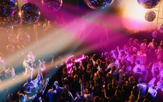 Ein Raum mit vielen Menschen bei einer Party mit bunten Leuchtstrahlern und Dekoration.