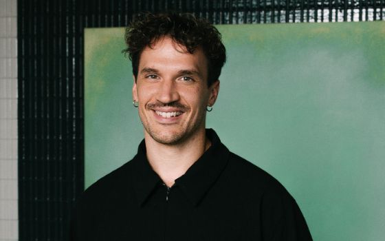 Porträt des Kochs Dominik Hartmann, ein junger Mann mit braunen Haaren in schwarzem Hemd vor grüner Wand.