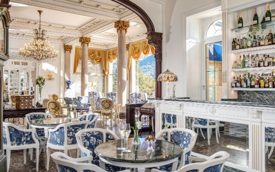 In einem Restaurant stehen Möbel im Barock-Stil vor einer Theke und an den Fenstern hängen opulente Gardinen. 