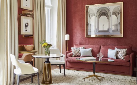 Edles Hotelzimmer mit hellen und burgunderroten Textilien sowie Einrichtungsgegenständen mit goldenen Akzenten.  