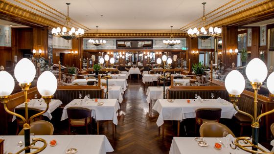 Edler Speiseaal im Brasserie-Stil mit Gold-Dekor und weiss eingedeckten Tischen.