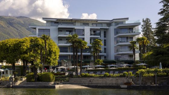 Weisse Fassade eines Hotels mit Balkonen, das von Bäumen umgeben ist und in einer Bergkulisse liegt.