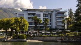 Weisse Fassade eines Hotels mit Balkonen, das von Bäumen umgeben ist und in einer Bergkulisse liegt.