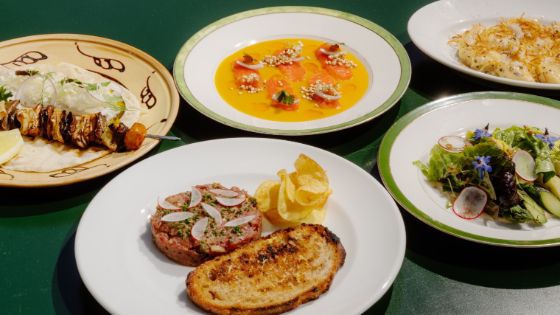 Fünf kunstvoll angerichtete Gerichte aus dem Restaurant Olympia in Bern auf einem grünen Tisch: darunter Rindstatar, Linsenchip, gegrillter Spiess, bunter Salat, Gnocchi und Lachs mit heller Sauce.