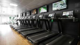 Mehrere Laufbänder mit Monitoren, aufgereiht an einer Wand in einem Fitnessstudio
